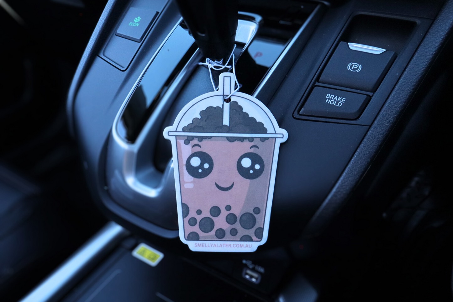 Cute smiling brown boba/bubble tea with black pearls and big sparkling eyes hung in a cool black interior car. Smell Ya Later - Scented Air Freshener. Suitable for homes, wardrobes, cupboards, bathrooms, cars, office space, pet rooms, bed rooms, kitchen.