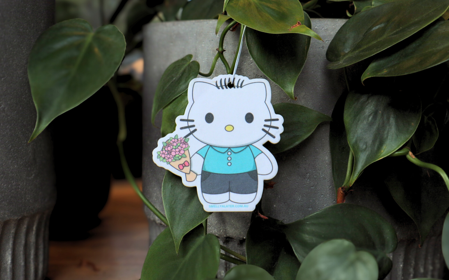 Cute Daniel Starr (Hello Kitty) with blue button shirt, black pants holding pink bouquet of flowers hanging on beautiful green plants. Smell Ya Later - Scented Air Freshener. Suitable for homes, wardrobes, cupboards, bathrooms, cars, office space, pet rooms, bed rooms, kitchen.