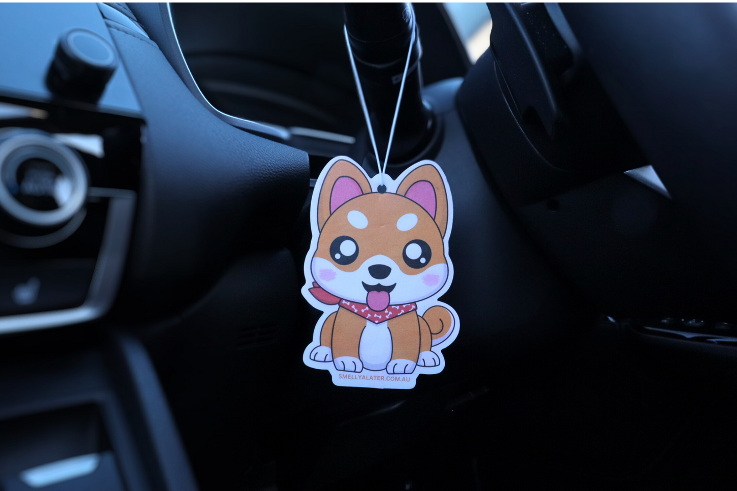 Cute chubby white and orange shiba inu poking its tongue with big sparkling eyes and wearing a red bandanna with white bone patterns, hung in a cool black interior car. Smell Ya Later - Scented Air Freshener. Suitable for homes, wardrobes, cupboards, bathrooms, cars, office space, pet rooms, bed rooms, kitchen.