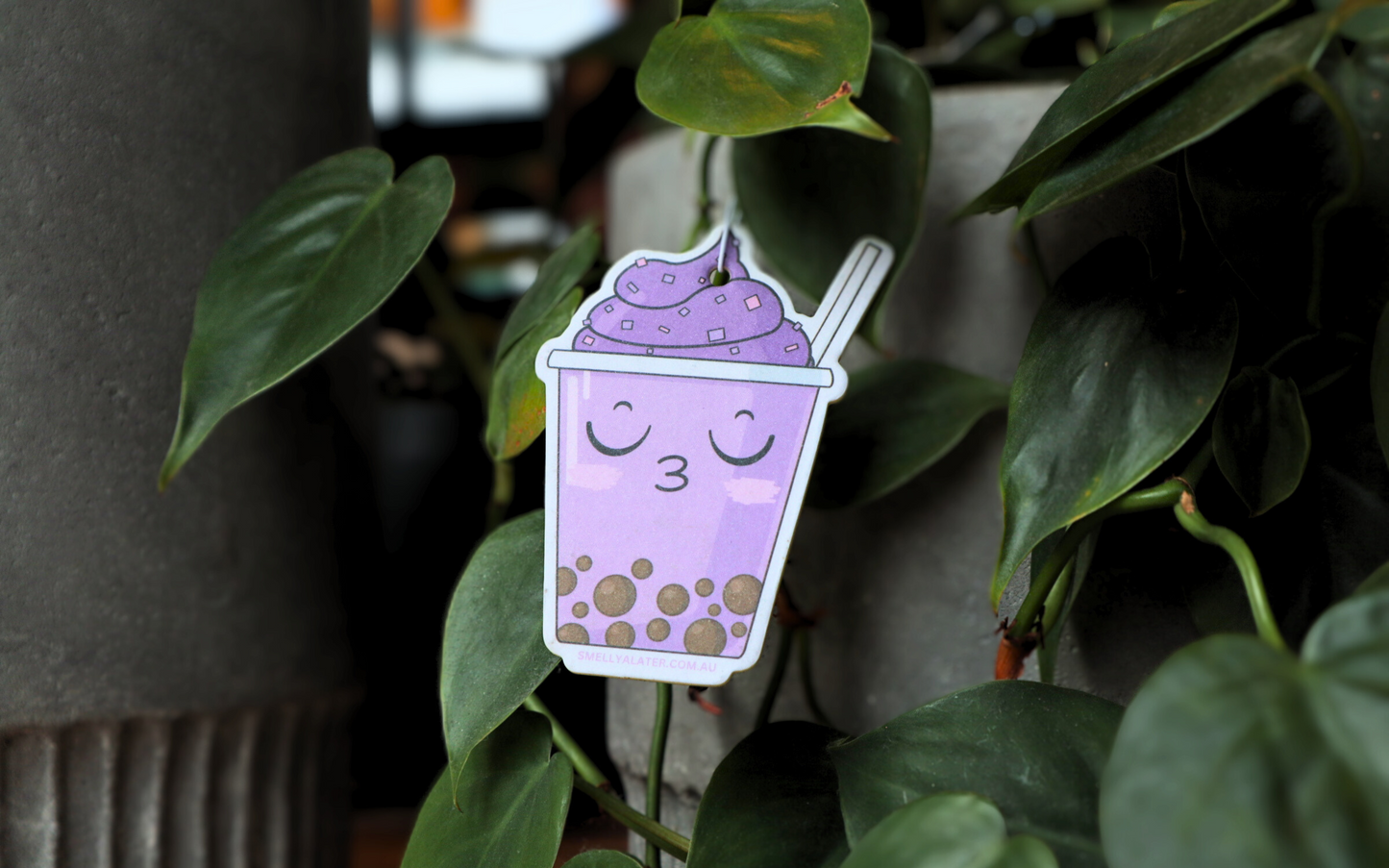 Cute, blushing kissy face purple boba/bubble tea with brown pearls, purple soft serve with sprinkles, hanging on beautiful green plants. Smell Ya Later - Scented Air Freshener. Suitable for homes, wardrobes, cupboards, bathrooms, cars, office space, pet rooms, bed rooms, kitchen.  