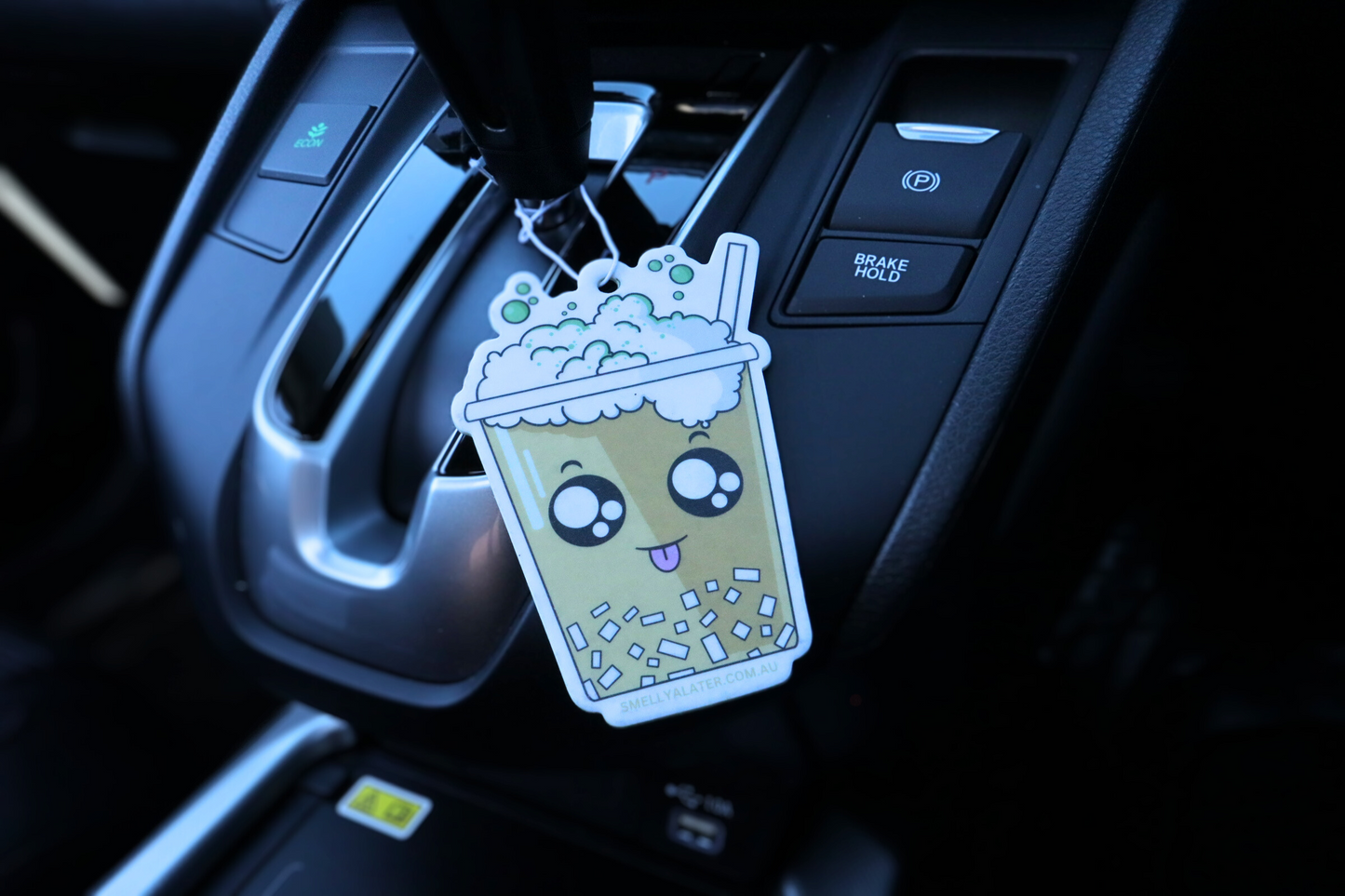 Cute, happy yellow boba/bubble tea poking its tongue with white bubbly froth, green sprinkles, white jelly and big sparkling eyes, hung in a cool black interior car. Smell Ya Later - Scented Air Freshener. Suitable for homes, wardrobes, cupboards, bathrooms, cars, office space, pet rooms, bed rooms, kitchen.  